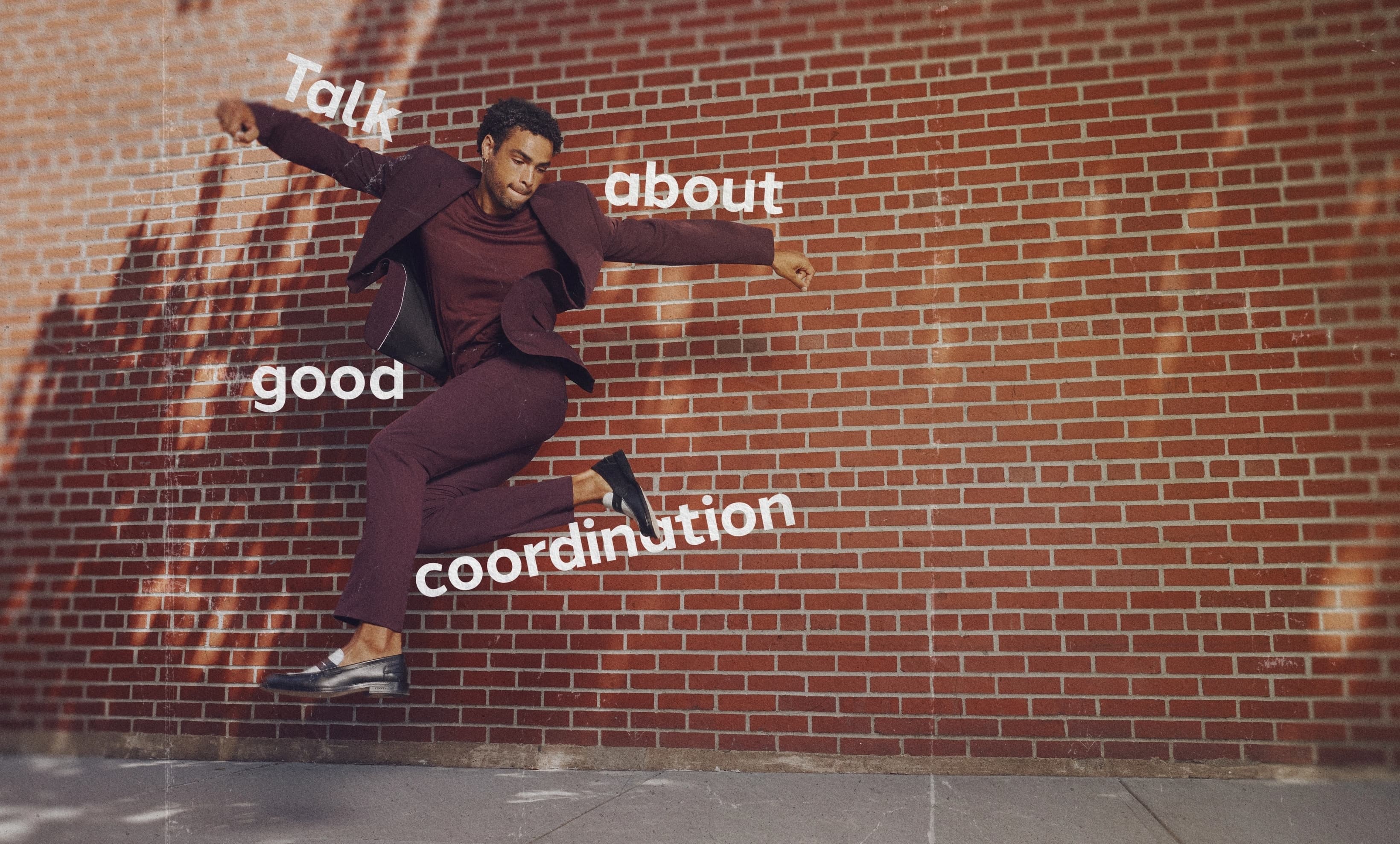 A young man wearing a burgundy suit dances down the street thanks to the stretchy material.