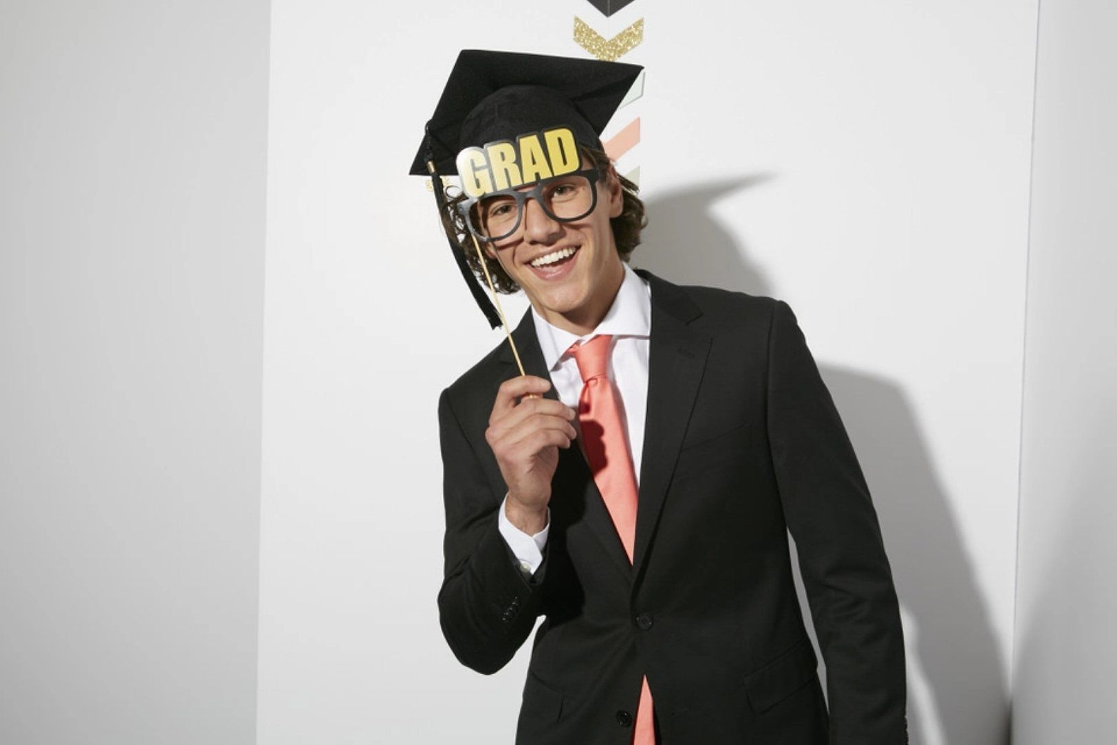 Guy at senior prom with photo booth props, salmon pink tie & black prom suit for high school graduation.