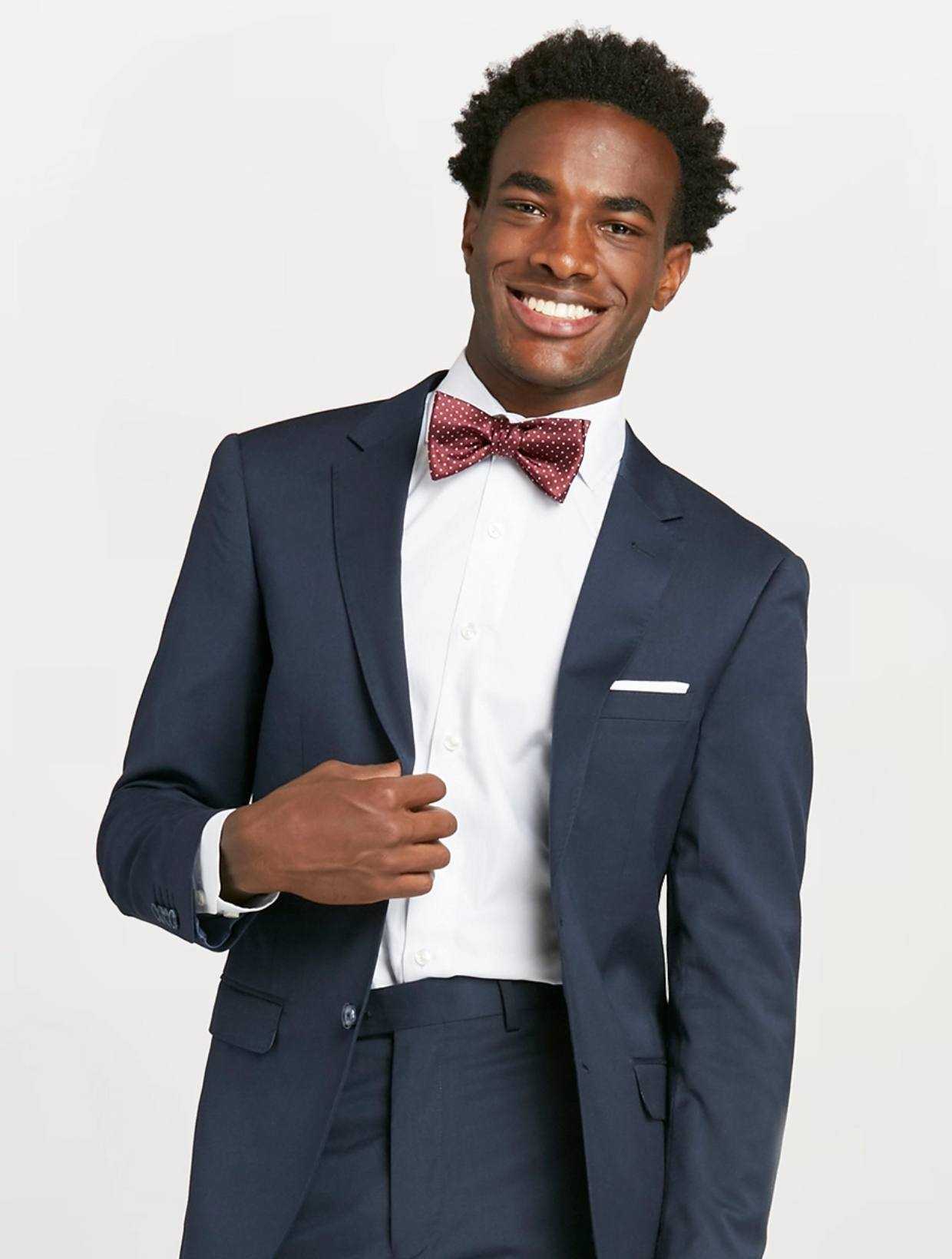 Guy at prom smiling in navy blue prom suit, maroon polka dot bow tie & pocket square.