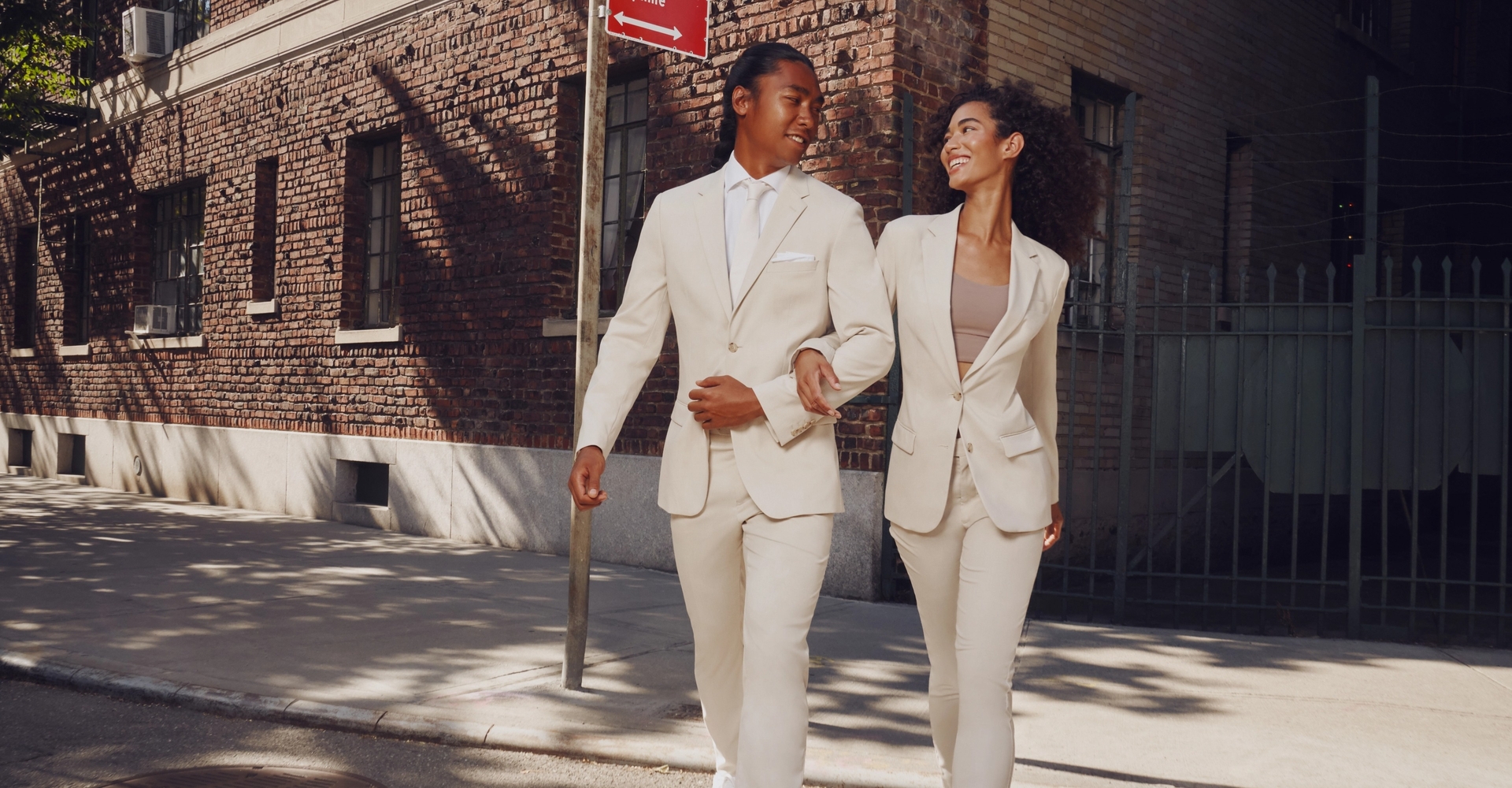 Couple in matching casual style men's and women's tan suits crossing city street.