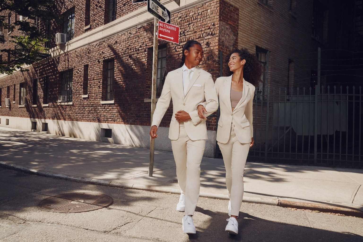 Young man and woman wearing SuitShop tan suits while walking across the street.