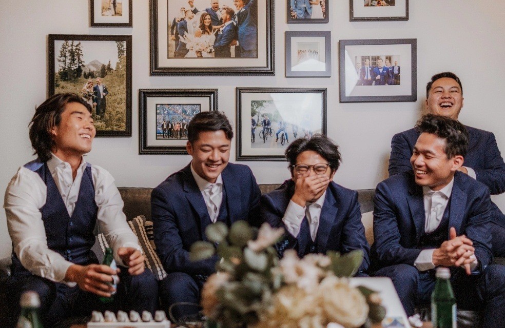 Guys in navy groomsmen suits laughing at modern suit store during group wedding fitting appointment.