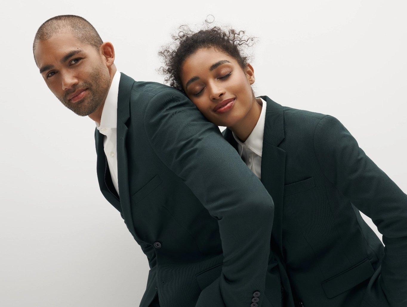 Man and woman in hunter green suits with dreamy facial expressions because of comfortable fitting suit.