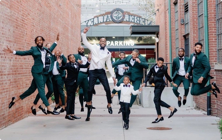 Green wedding party jumping in hunter green suits, patent loafers, & bow ties alongside black & white tuxedos.