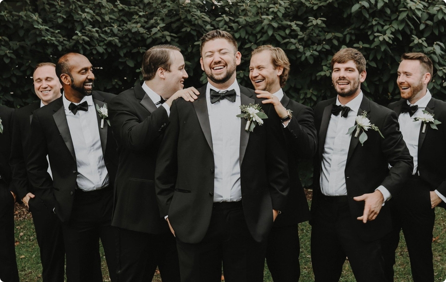 Black tie groomsmen standing behind groom in black notch lapel tuxedo from suit store in Denver.