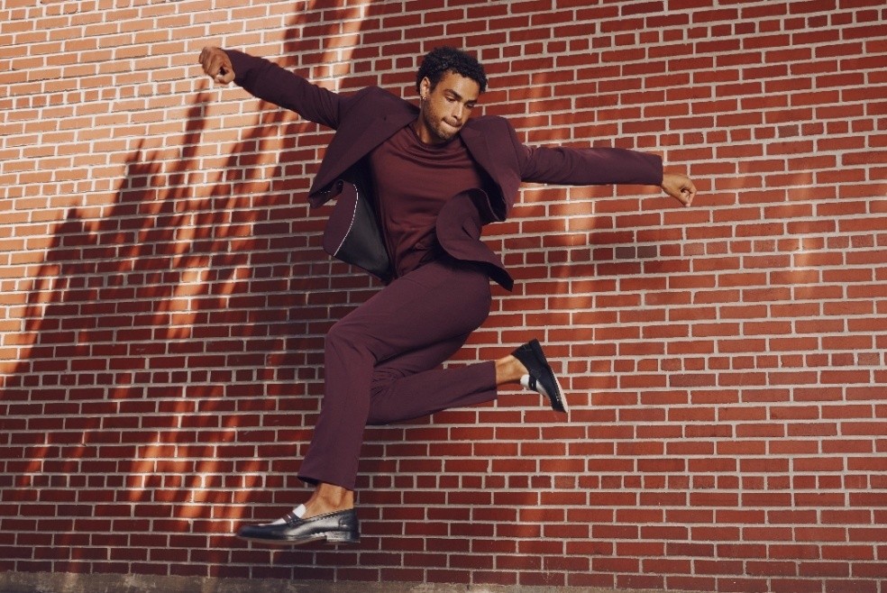 A man in a burgundy suit jumps and dances freely and easily.