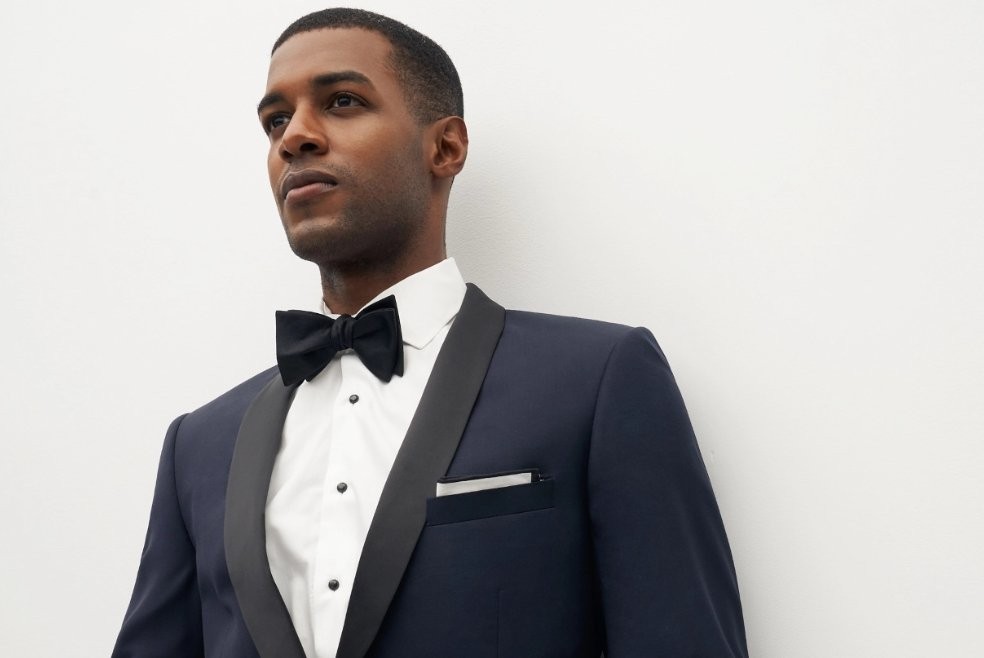A man in a navy tuxedo and black bowtie looks away from the camera.