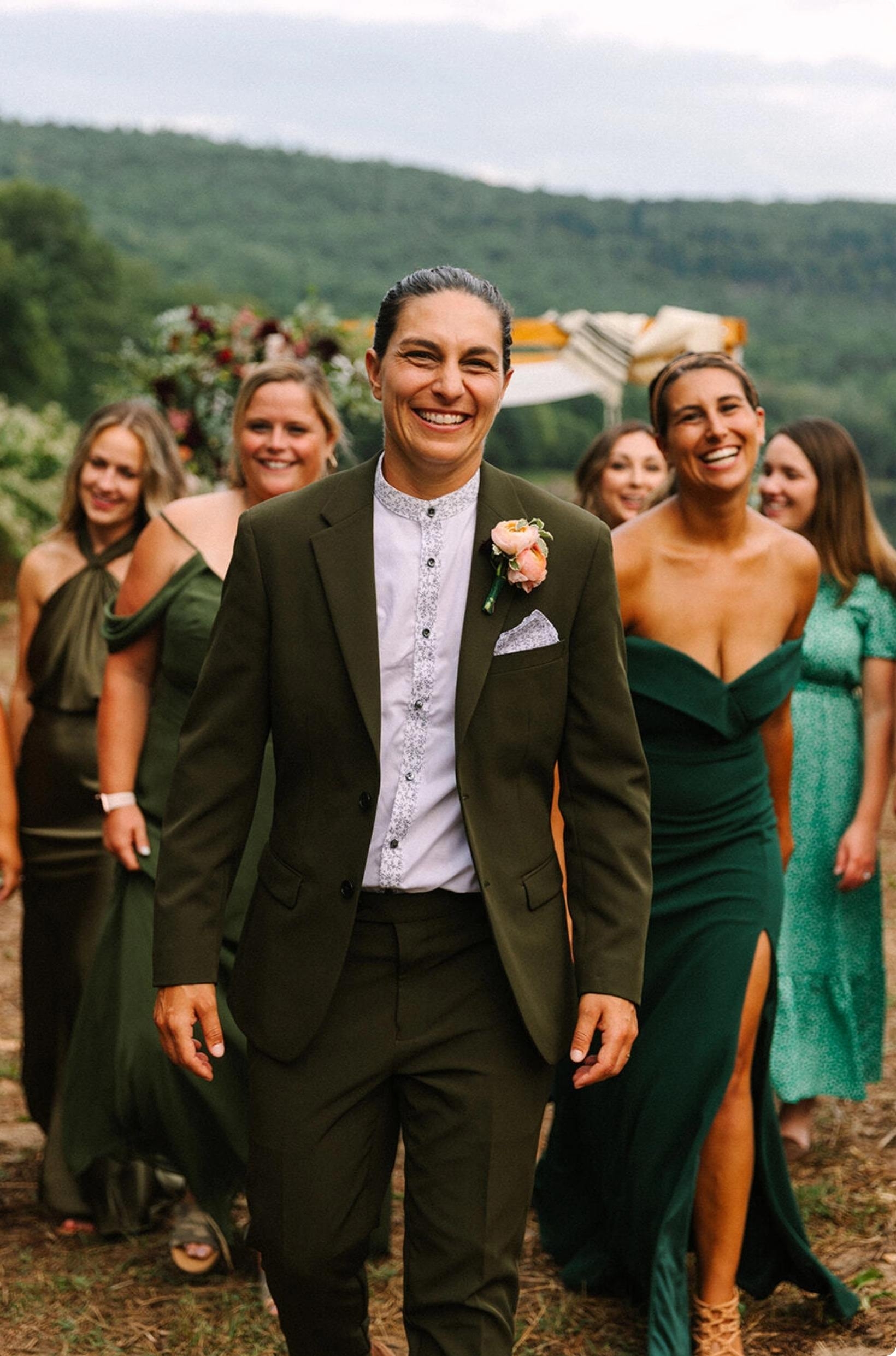 Bride wearing unique olive women's suit with collarless patterned dress shirt at outdoor wedding with green, marigold & maroon color scheme.