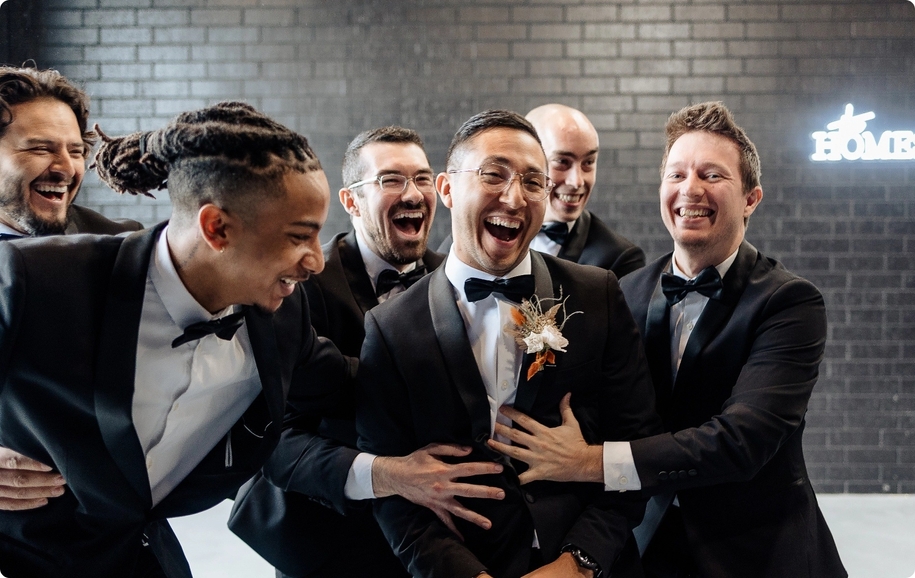 Houston black tie wedding laughing in shawl lapel black tuxedos with pop of orange in florals.