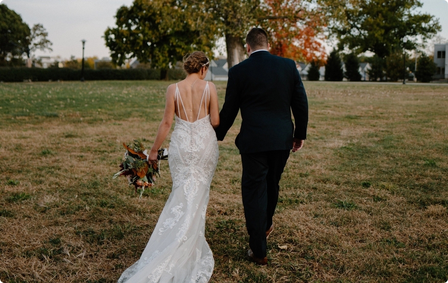 Chicago fall wedding behind shot of bride in lace gown and groom in green suit walking.