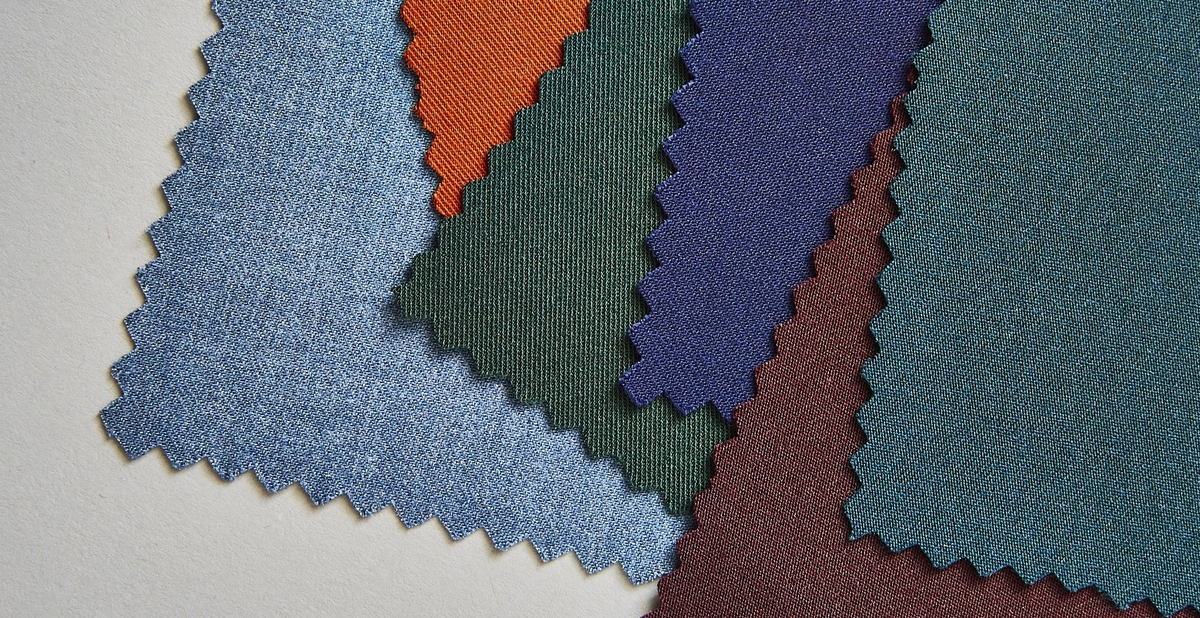Fanned suit fabric swatches in light blue, burnt orange, rust color, dark green, burgundy, & deep teal.