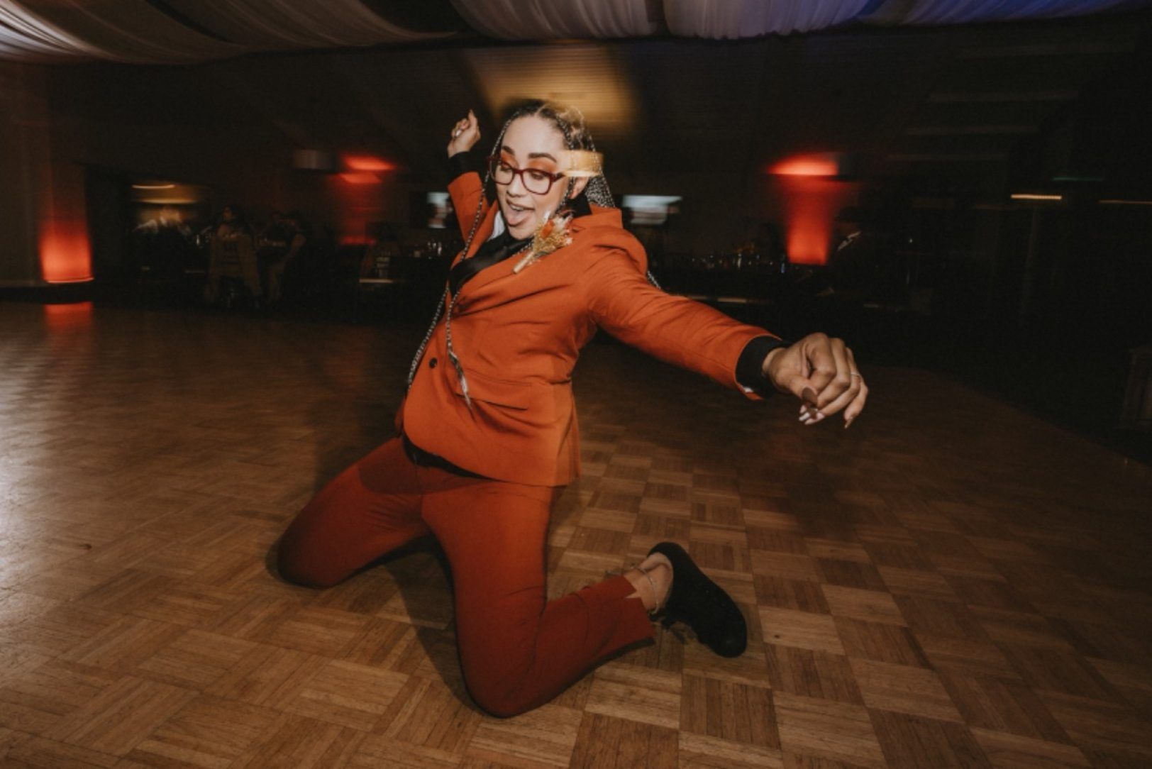  Bold girl's suit prom style in burnt orange pants outfit for prom sliding on dance floor.