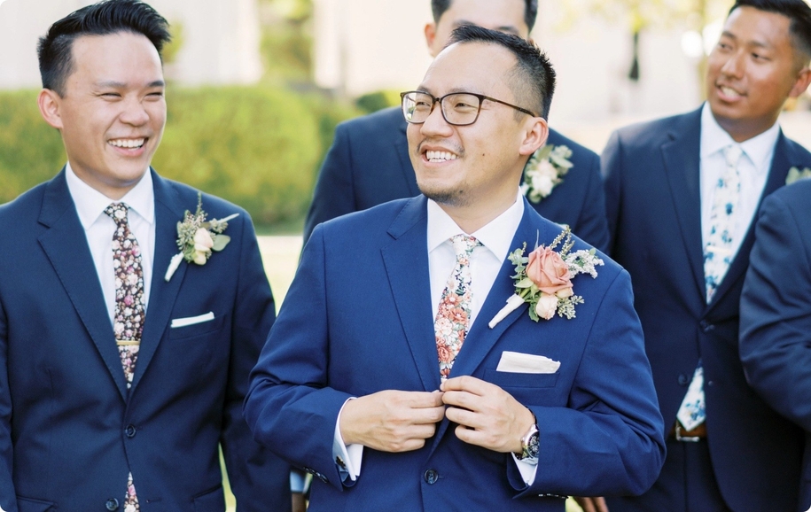 Smiling brilliant blue groomsman party wearing royal blue suits, blush pink rose boutonnieres, & floral neck ties.