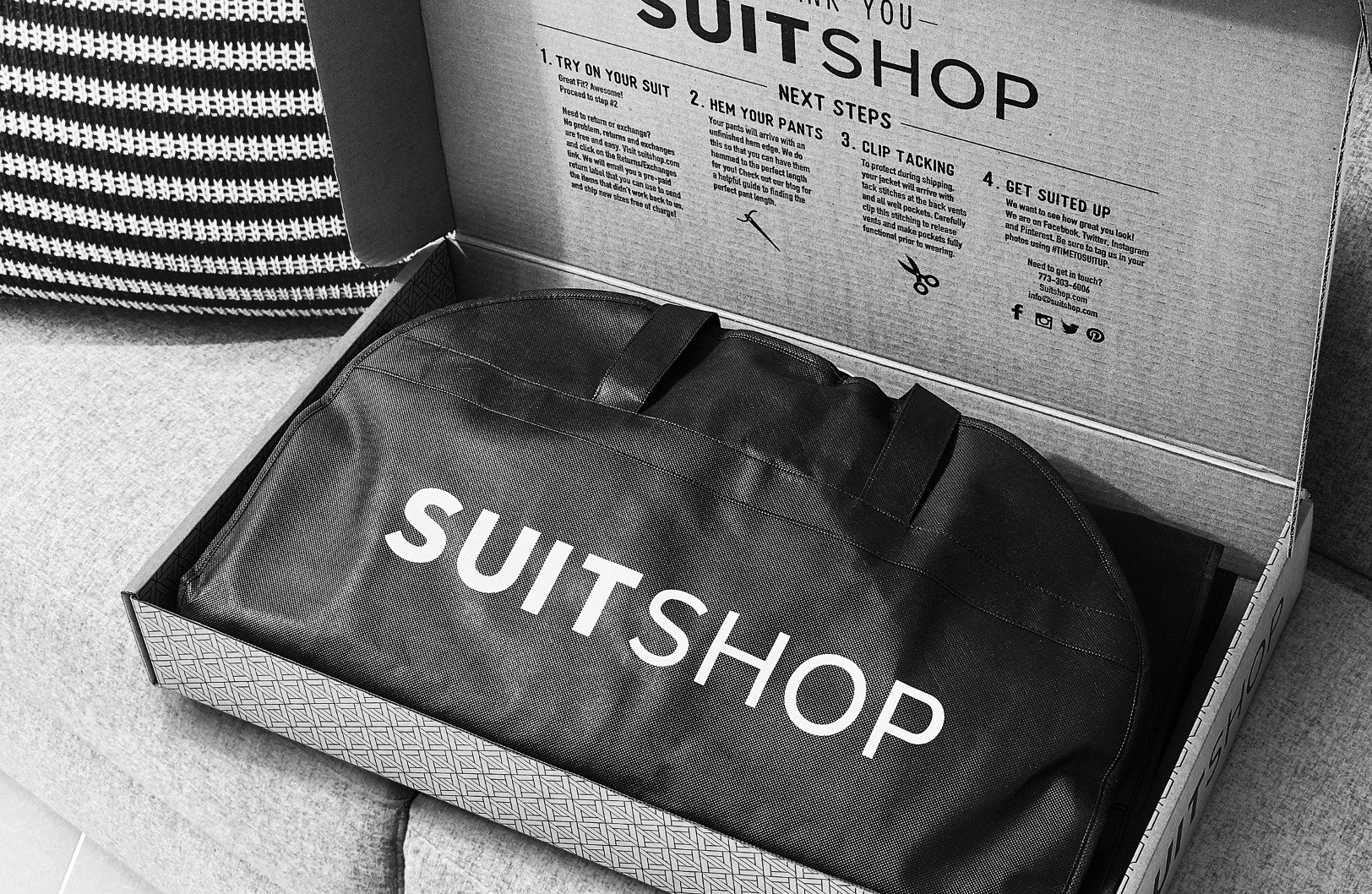 SuitShop delivery box open showing written next steps and suit garment bag in black and white.