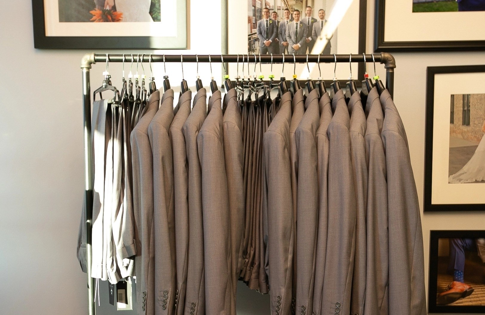 Grey suit jackets & pants in front of wedding photo gallery wall at suit store in Boston.