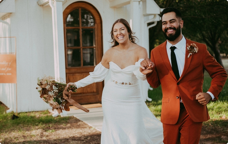 Houston chapel wedding with puff sleeve wedding gown bride, burnt orange wedding suit groom, & rustic flowers.