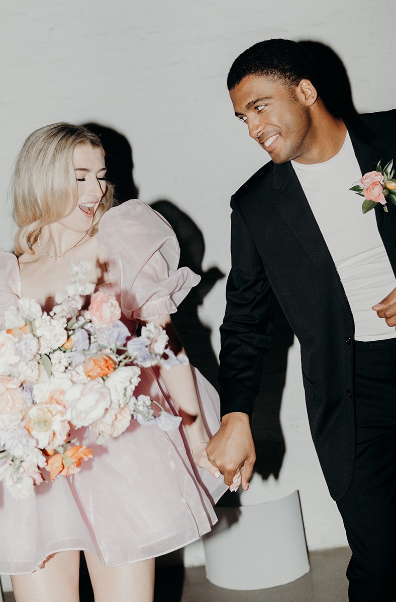 Romantic shoot with a black wedding suit, short blush gown, and soft flowers.