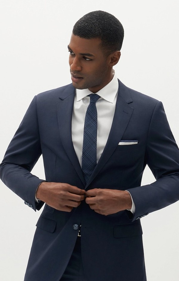 Man buttoning navy blue suit jacket wearing a matching navy tie.
